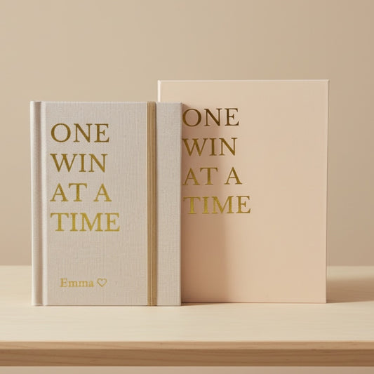 Inwords Gifting One Win at a Time notebook with a hardcover and motivational quote on the cover, shown in a clean, minimalist setting.
