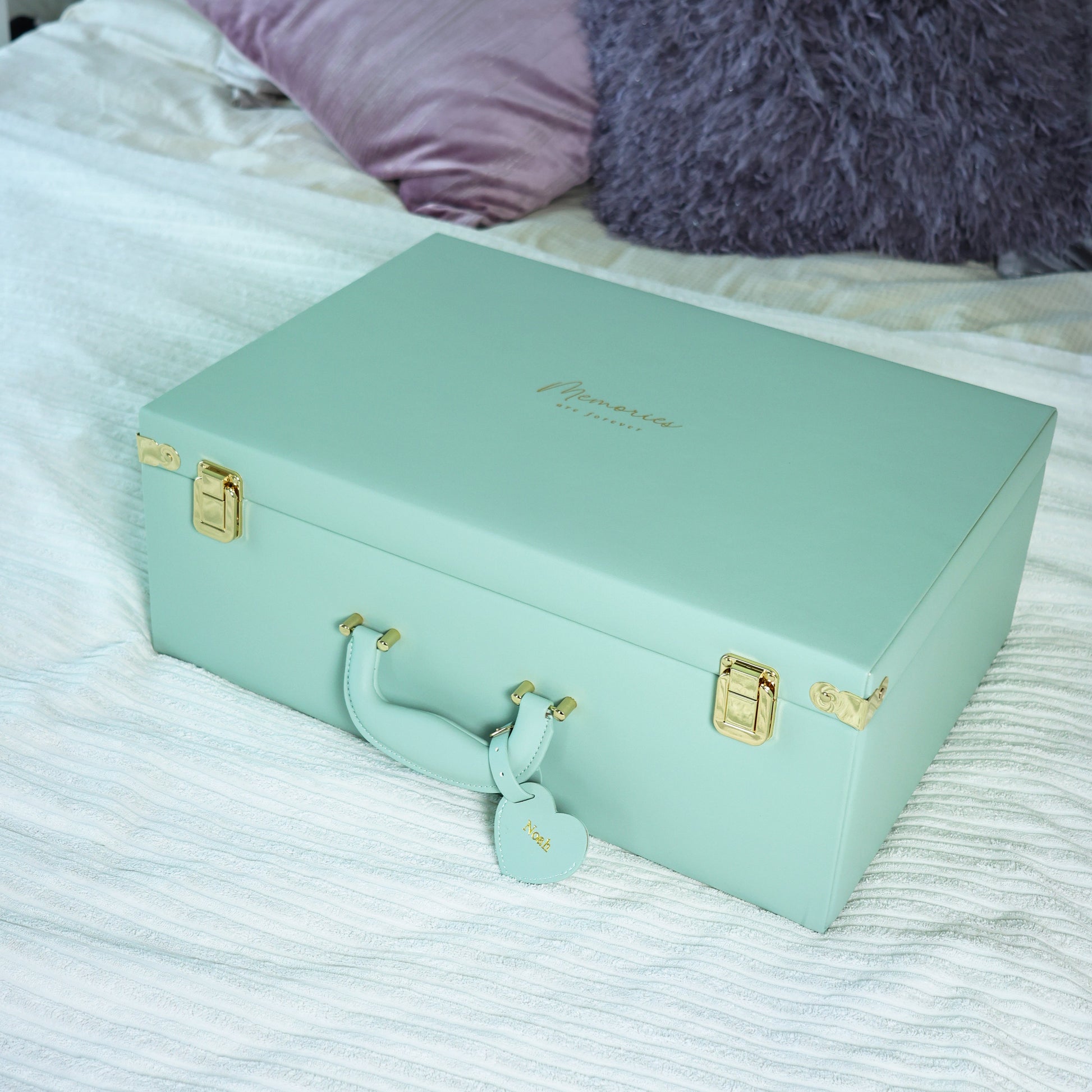 Mint green suitcase with gold accents on a bed with purple pillows