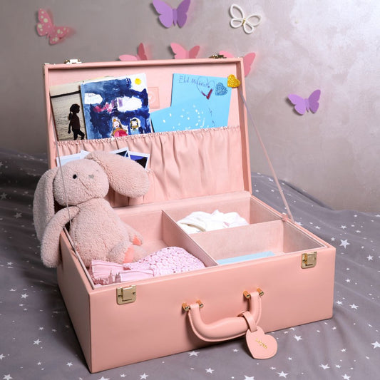 Pink storage box with a teddy bear, photos, and baby items on a bed with butterfly decorations.