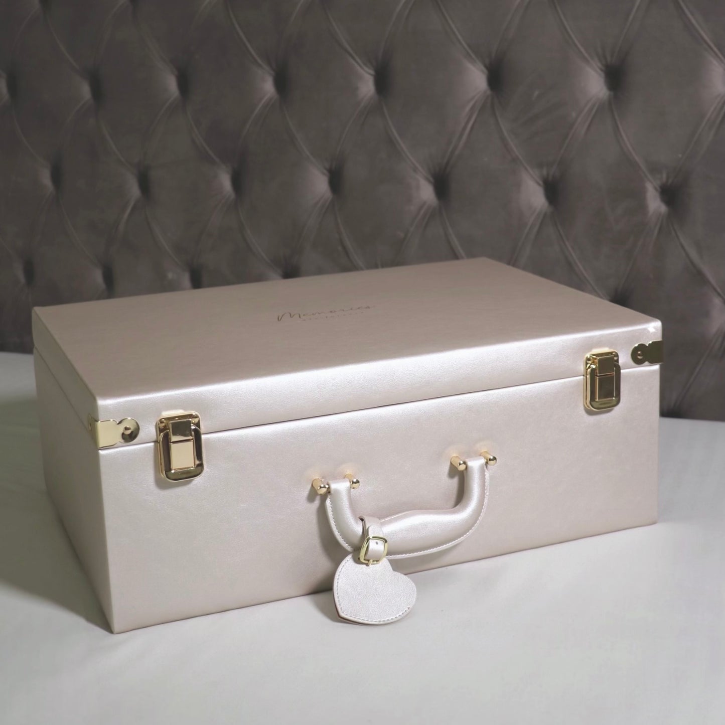 White memory box with gold accents on a gray surface against a textured gray wall.
