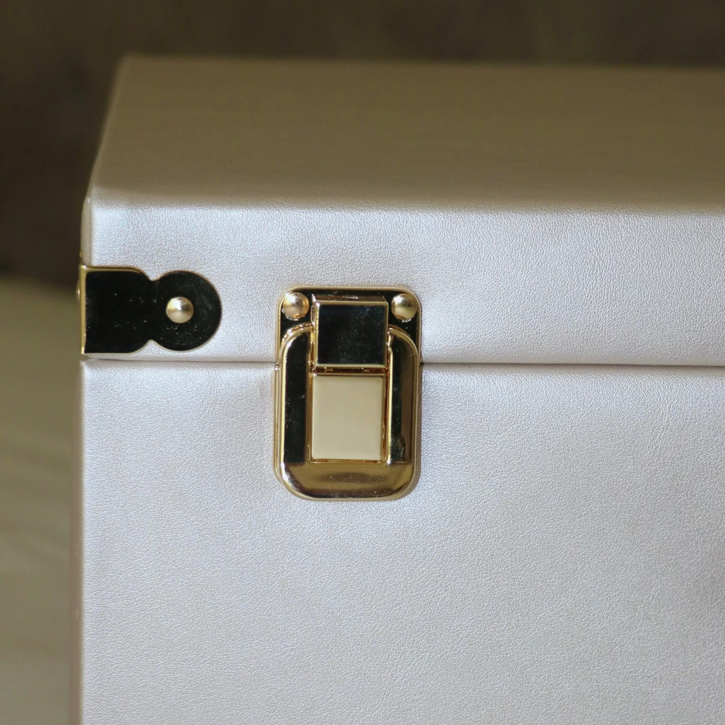 Close-up of a white suitcase with gold latch on a neutral background