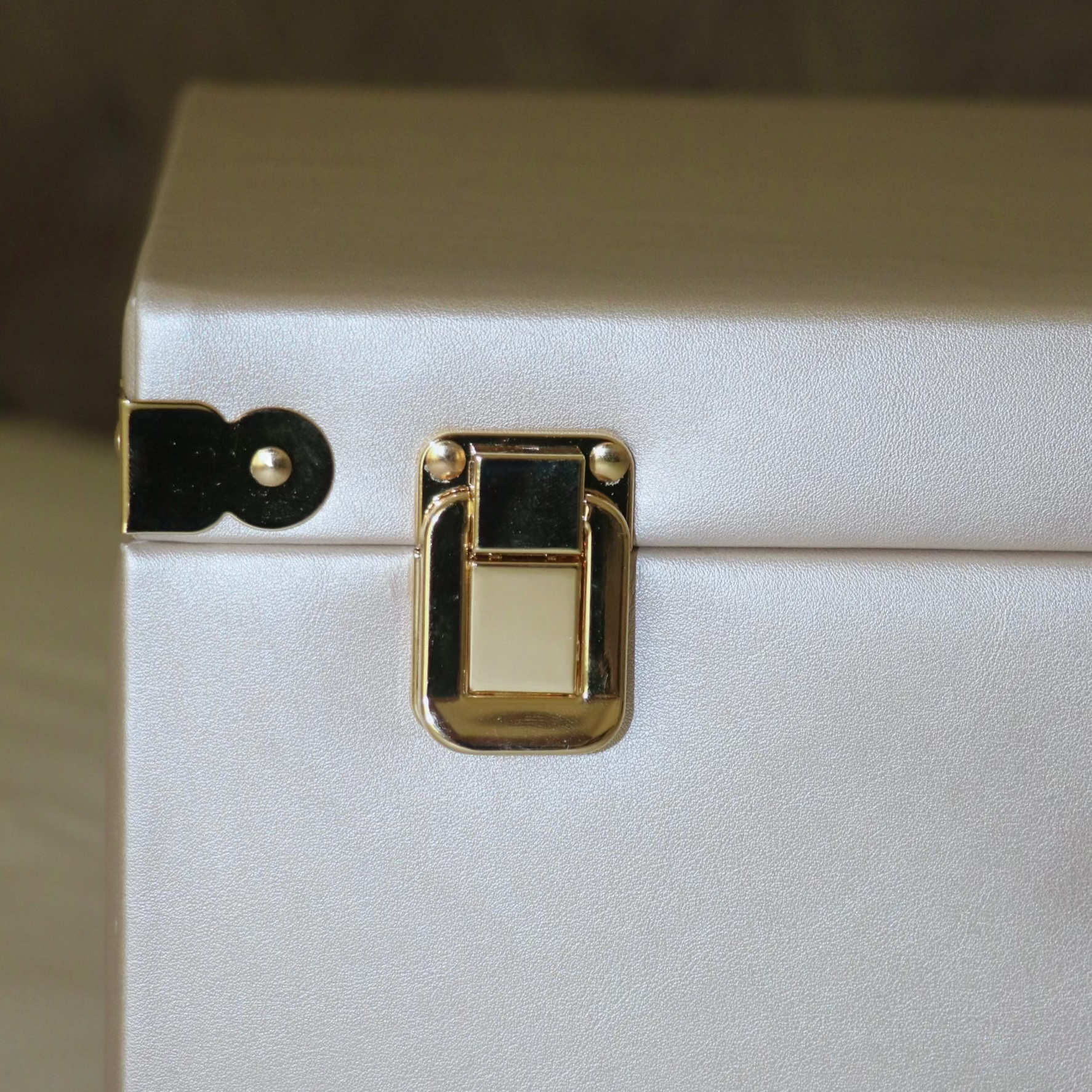 Close-up of a white suitcase with gold latch on a neutral background