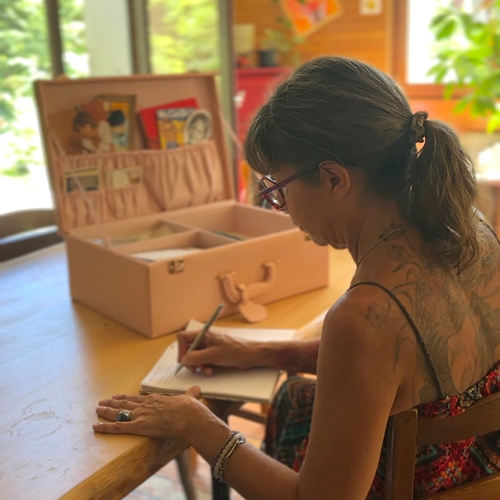 A woman writing beside an open blush Memory Keepsake filled with photographs